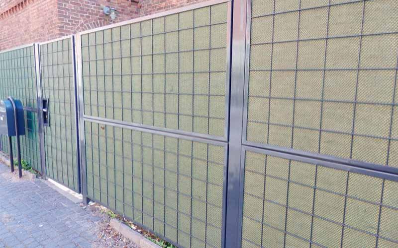 Grønt støjhegn med dør ved lejlighedskompleks